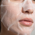 Närbild av Vitamin C Sheet Mask i tygmaterial med nätstruktur på kvinnas ansikte