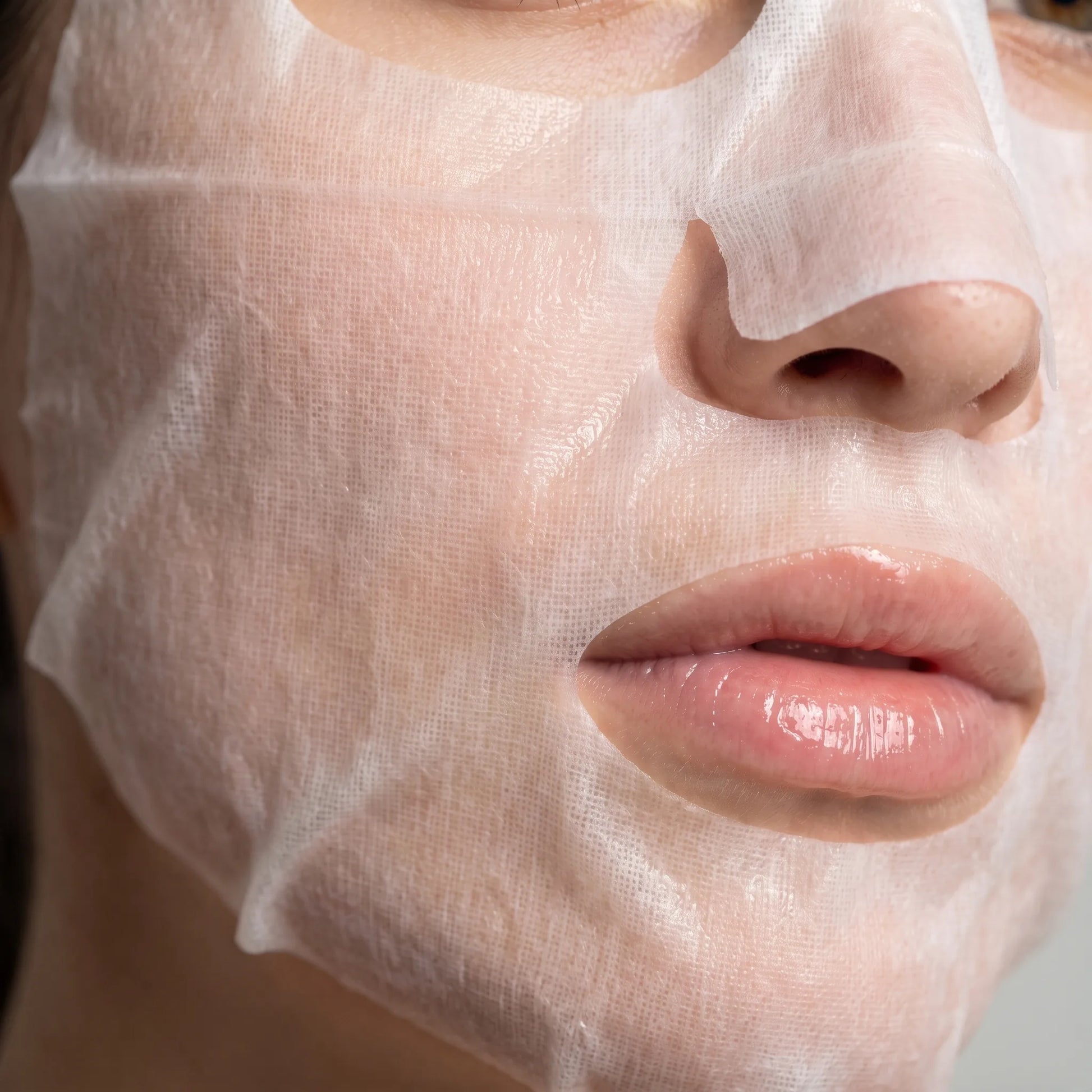 Närbild av Vitamin C Sheet Mask i tygmaterial med nätstruktur på kvinnas ansikte